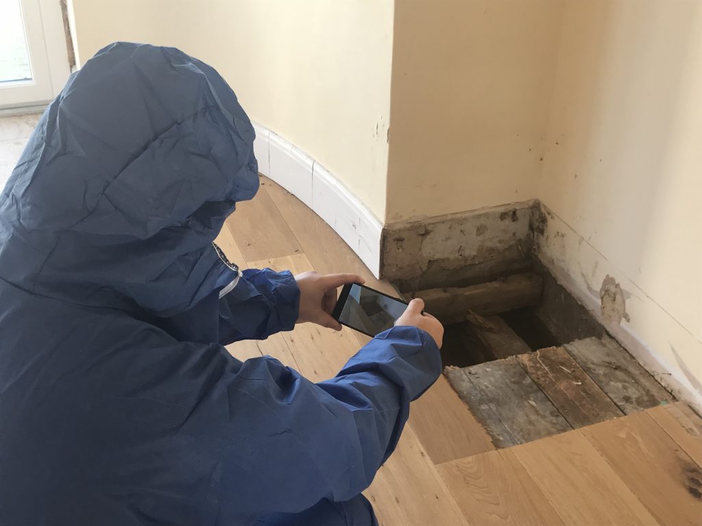 Surveyor in protective overalls photographing an opening in a wooden floor